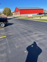 Parking lot by Jerry Greier sign and large red and gray building.