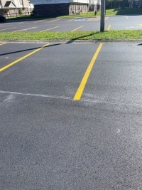 Resurfaced parking lots by apartment buildings with a strip of grass between them.