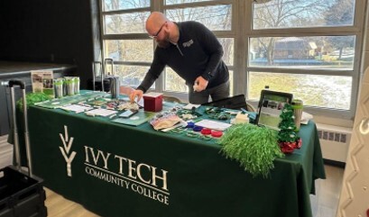 A man behina table covered with information for Ivy Tech Community College.